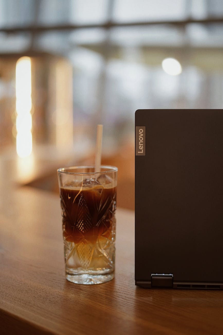 shallow focus photo of glass of coffee beside a laptop